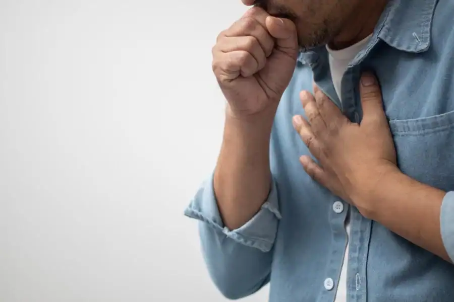 A close-up of a man’s hand on his chest while he’s coughing into a fist.